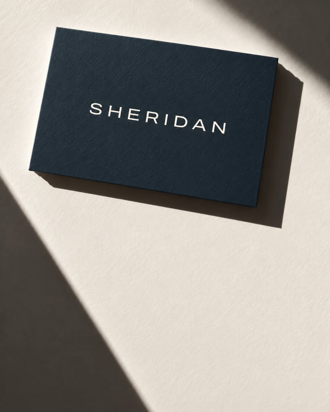 A navy Sheridan business card on linen paper in raking sunlight